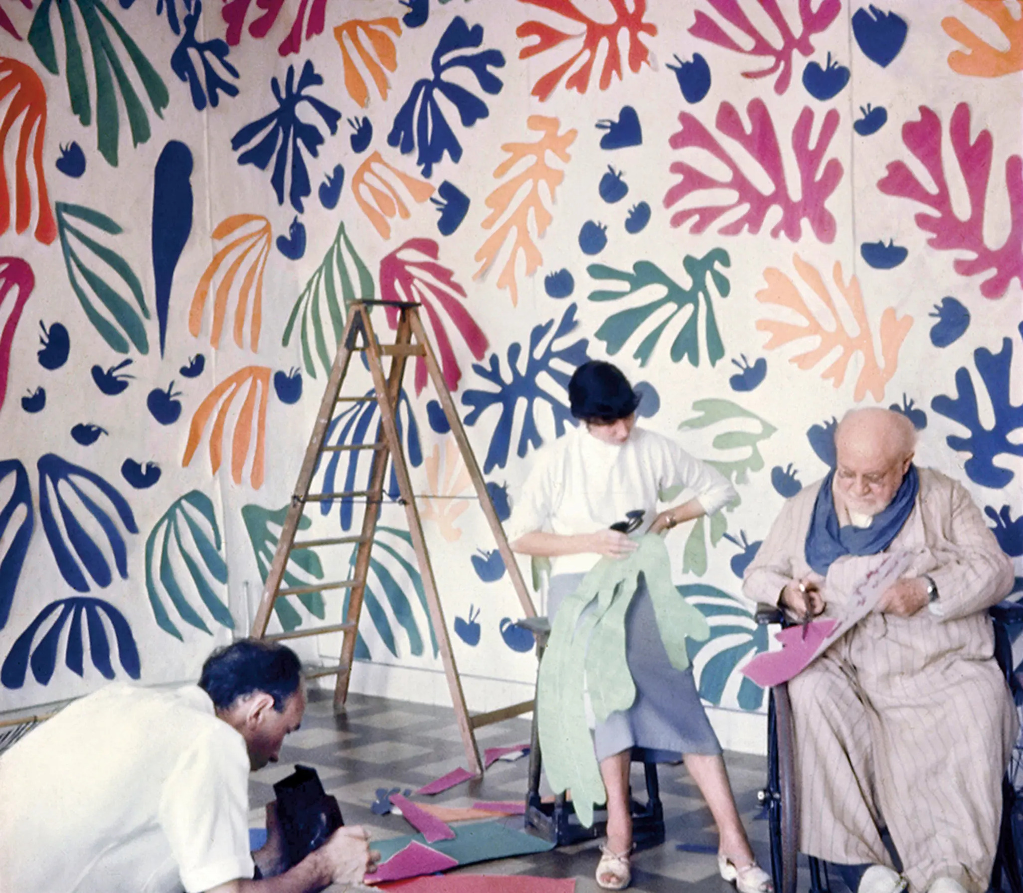 Photographie de Henri Matisse travaillant aux gouaches découpées dans son atelier, entouré d’assistantes, illustrant comment la création par la couleur et le geste se poursuit malgré la fatigue et la maladie.